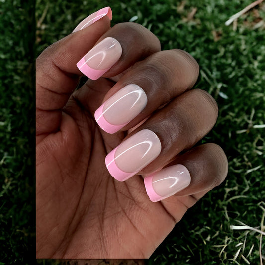 Hand with short square pink French tips press-on nails on a green grass background