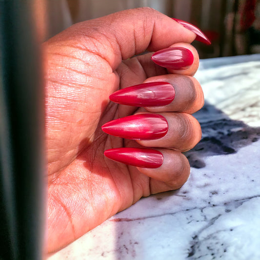 Long glossy maroon stiletto press-on nail on a white background