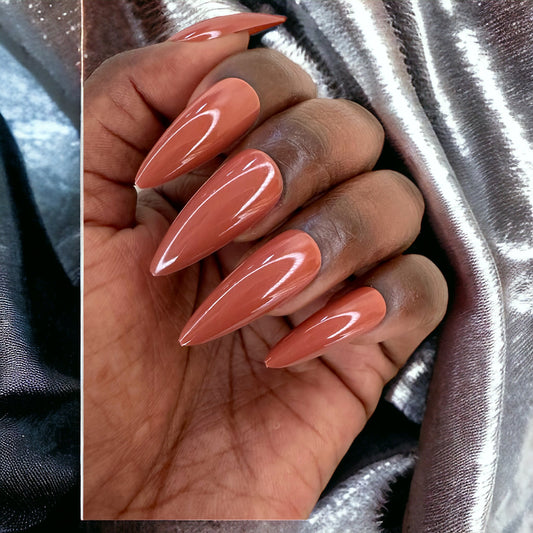 Hand with caramel-colored long stiletto-shaped press-on nails against a shiny silver background