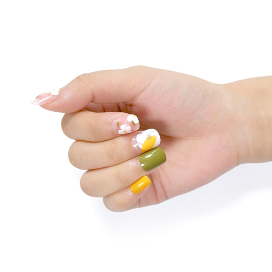 Hand against a white background with short square press on nails tips, colors white, green and yellow.