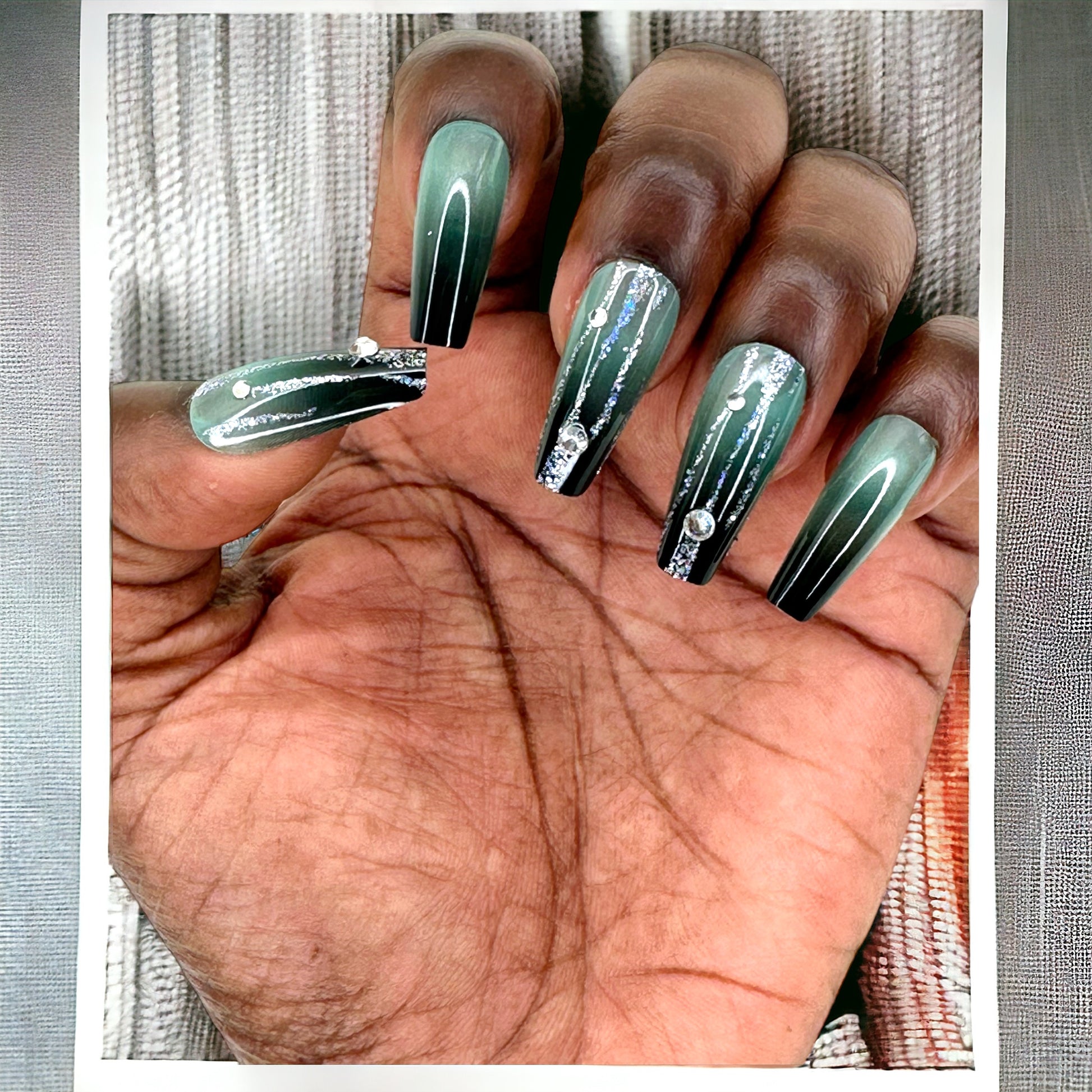 Hand adorned with long coffin-shaped press-on nails in green Ombre color with rhinestones