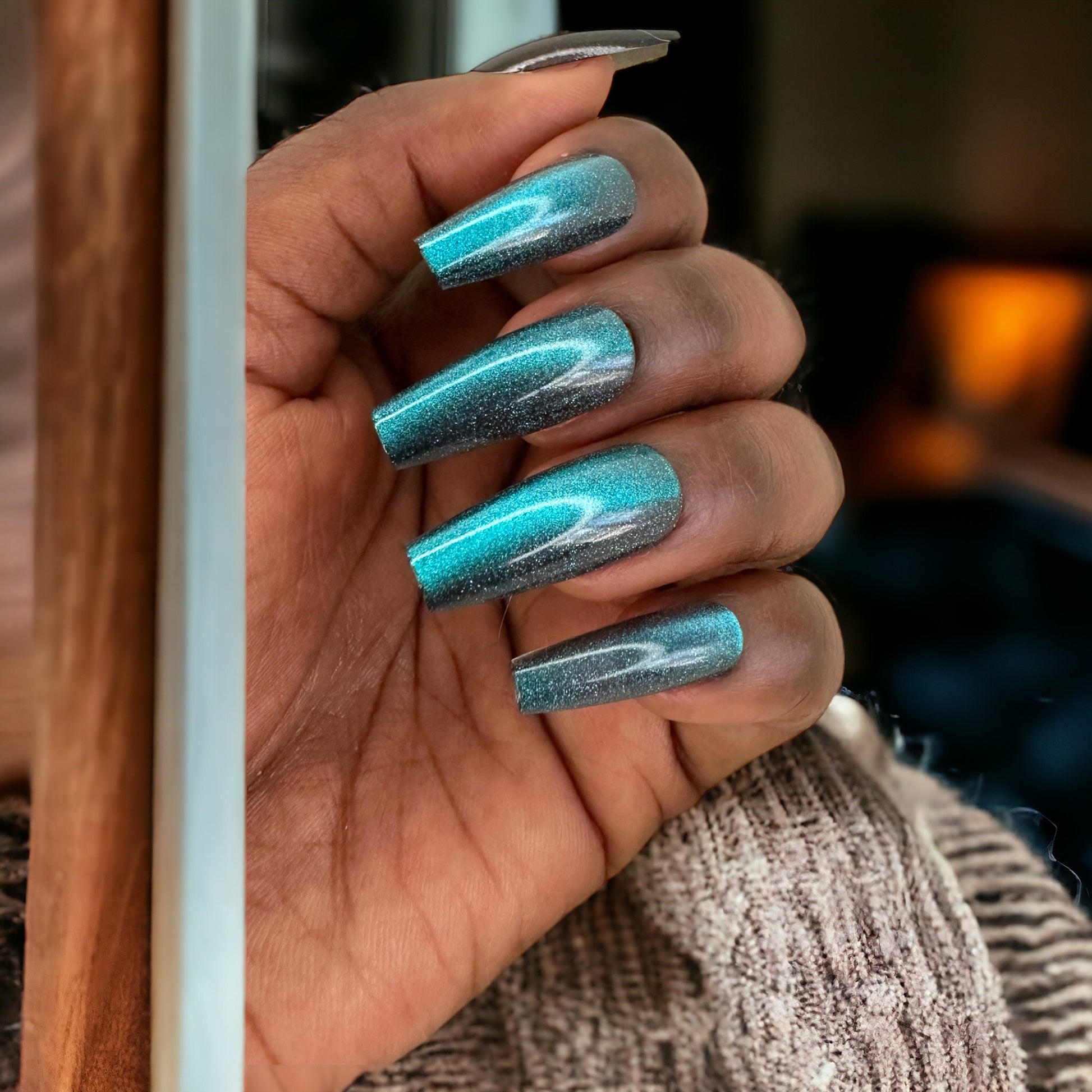 Hand featuring teal cat eye color long coffin shape press-on nails against a neutral background