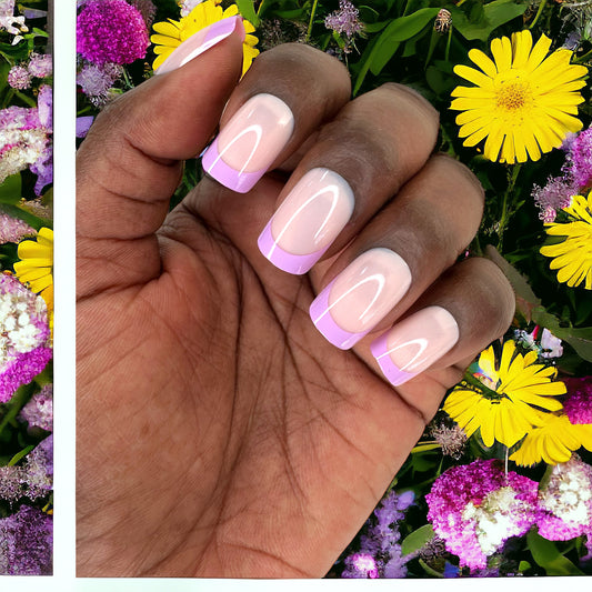 Hand with fingers adorned with short square press-on nails featuring pink and purple French tips against a colorful flower background