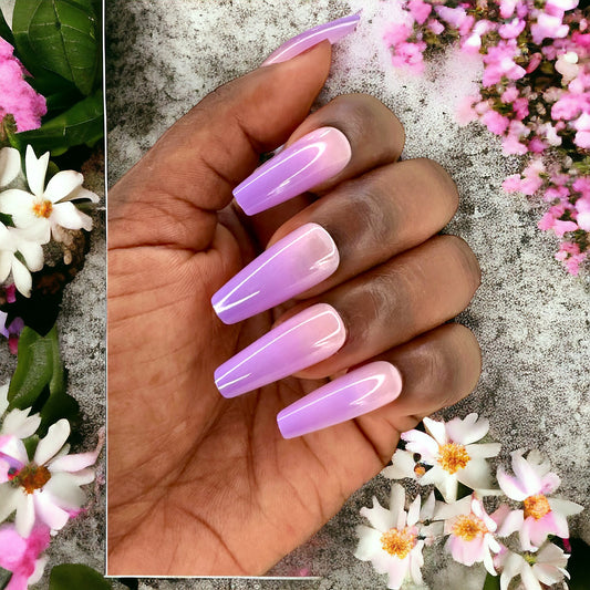 Hand with long coffin-shaped press-on nails in violet color against a backdrop of pink and white flowers