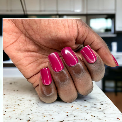 Hand adorned with short square press-on nails in dark fuchsia color