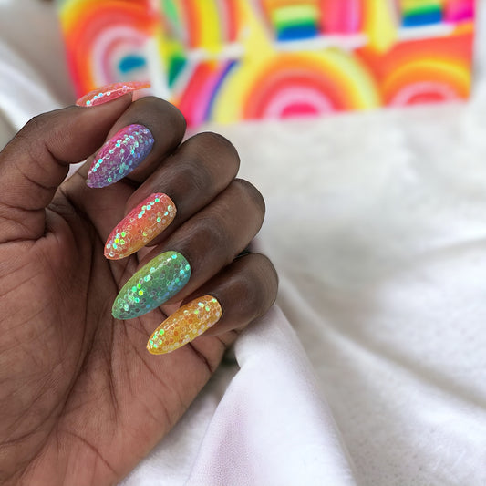 A hand adorned with almond-shaped press-on nails in a vibrant rainbow of colors, resting on a white fabric