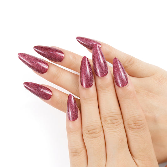 Two hands showcasing almond-shaped press-on nails in matte burgundy, set against a plain white background